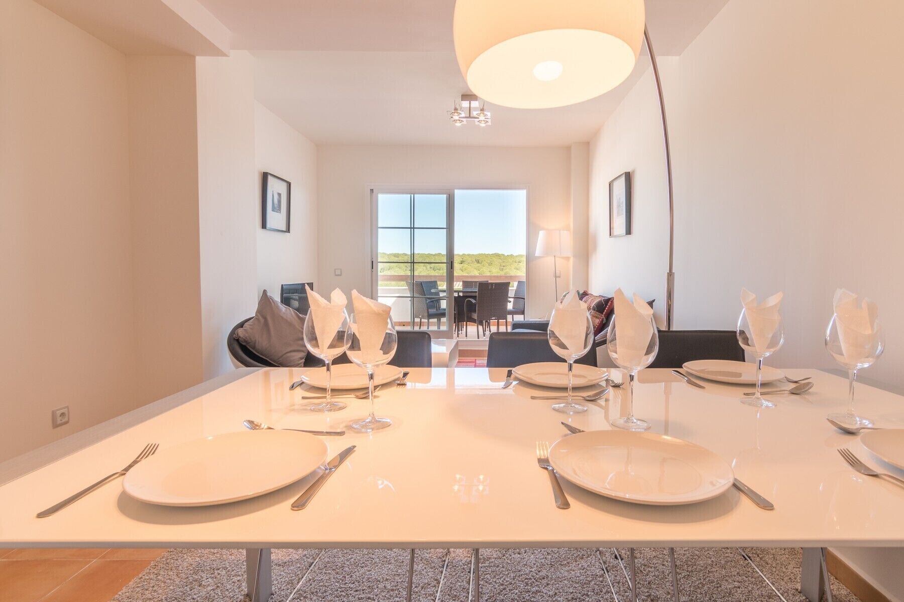 A dining area with a large table set for six, equipped with plates, cutlery, and wine glasses.