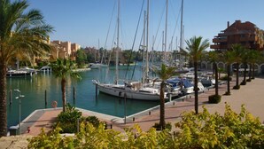 A marina with multiple sailboats docked, surrounded by palm trees and buildings.