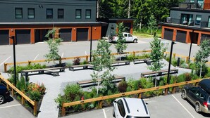 A parking lot with multiple cars, a small building, and a fenced garden area. - Perfect for your Winter and Summer Vacations! (Revelstoke)