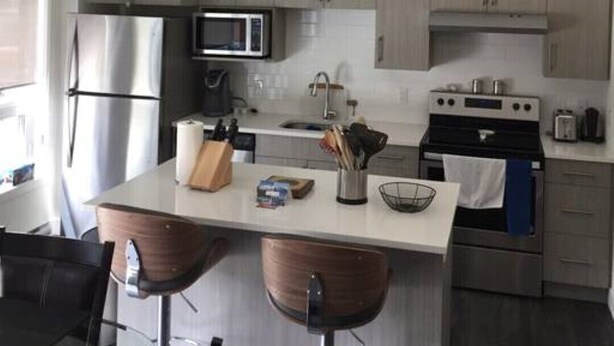 A modern kitchen with stainless steel appliances, wooden bar stools, and pendant lighting. - Perfect for your Winter and Summer Vacations! (Revelstoke)