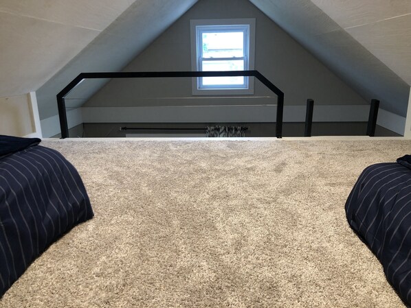 A bedroom with a sloped ceiling, a window, and a bunk bed with striped bedding.
