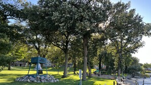 Ein Park mit einer Bank, einem Schild mit der Aufschrift 'Bell Harbor' und einem Spielplatz.