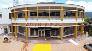 A multi-story building with a yellow and white color scheme, featuring a large entrance with glass doors and a sign in a foreign language.