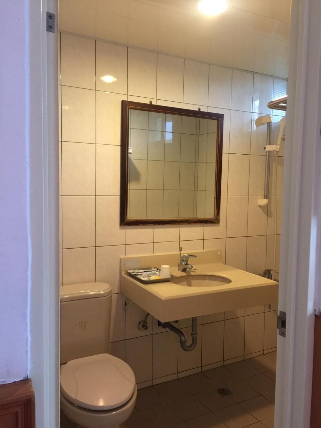 A small, clean bathroom with a toilet, sink, and mirror.
