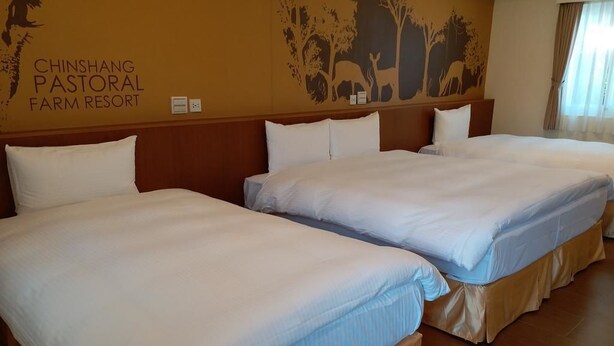 A hotel room with two beds, a mural of animals, and the name 'CHINSHANG PASTORAL FARM RESORT' on the wall.
