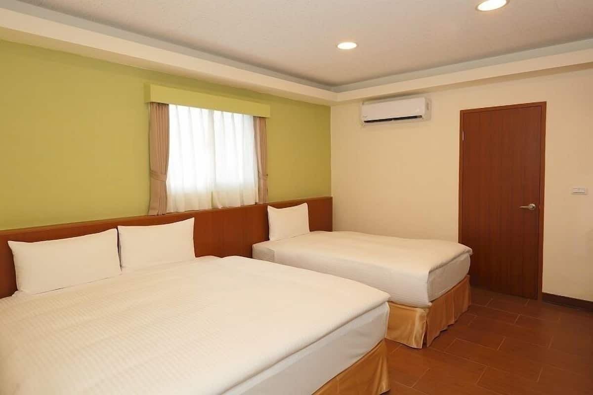 Habitación de hotel con dos camas, una ventana con cortinas, un equipo de aire acondicionado y una puerta de madera.