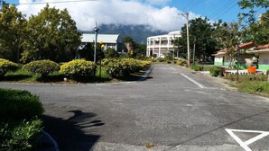 A street with a clear road, a white building with a curved roof, and lush greenery.