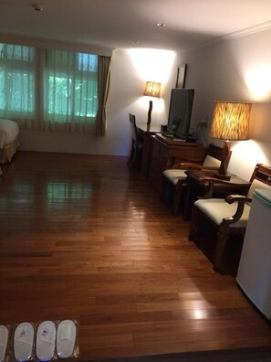 Een hotelkamer met een houten vloer, een bed, een bureau met een computer, twee lampen en een televisie.