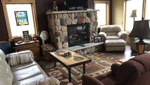 A cozy living room with a stone fireplace, leather sofas, a coffee table, and a television. - NEWER FAMILY 3 BEDROOM 2 BATH LAKE CABIN (Swan River)