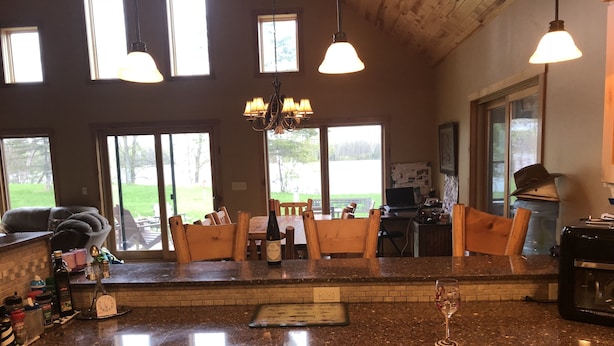 A kitchen with wooden cabinets, a granite countertop, and a chandelier. There are windows providing natural light and a view of the outdoors. - NEWER FAMILY 3 BEDROOM 2 BATH LAKE CABIN (Swan River)