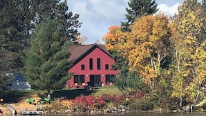 A red house with a porch, surrounded by trees and a lake. - NEWER FAMILY 3 BEDROOM 2 BATH LAKE CABIN (Swan River)