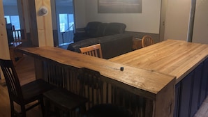 A kitchen with a wooden counter, a dining table, and chairs. There is a black leather sofa in the background. - Best Location on the MIssouri River (Cascade)