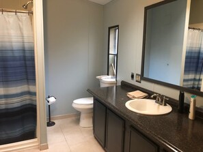 Een badkamer met douche, toilet, wastafel en spiegel.