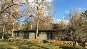 A small, single-story cabin with a metal roof, surrounded by a grassy yard and trees. - Best Location on the MIssouri River (Cascade)