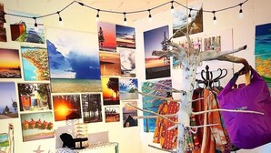 Ein Zimmer mit Wand, die mit verschiedenen Landschaftsbildern dekoriert ist, einem Stuhl und einem Gestell für Taschen und Kleidung.