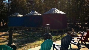 Jurten mit Schornstein, Sitzgelegenheiten im Freien und bewaldeter Hintergrund.