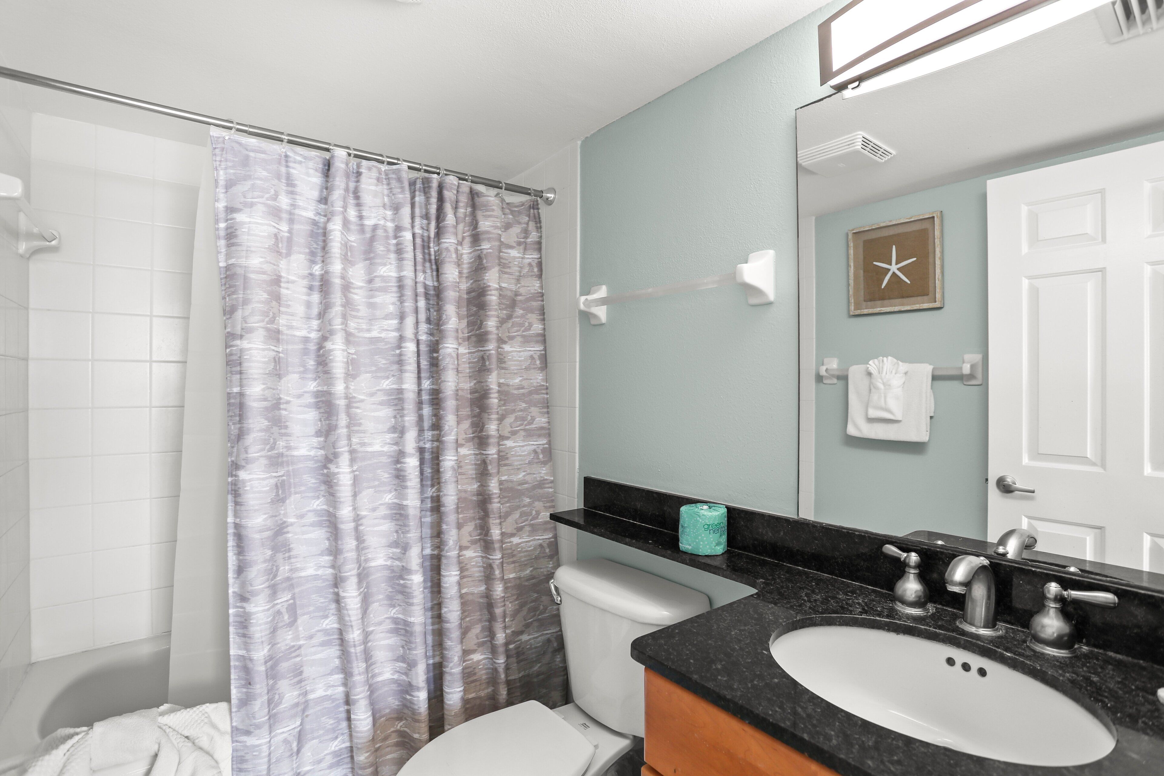 A bathroom with a shower curtain, toilet, sink, and a towel rack.