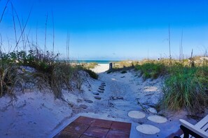 Ein sandiger Pfad führt zu einem Strand unter blauem Himmel.