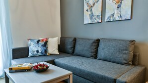 Una sala de estar moderna con un sofá seccional gris, una mesita con libros y un bol de fruta, y dos cuadros de ciervos colgados en la pared.