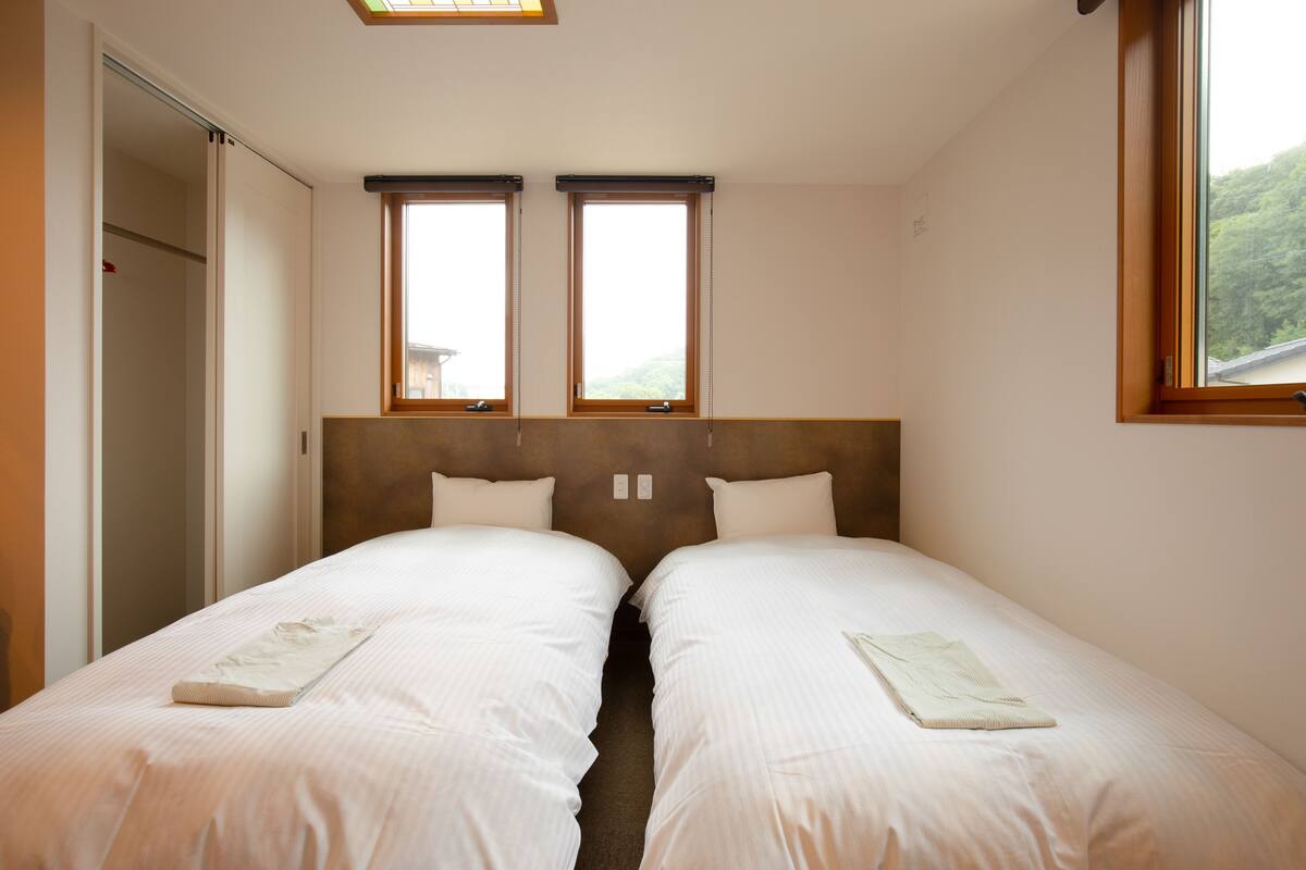 A hotel room with two single beds, a wooden headboard, a skylight, and a view of the outdoors.