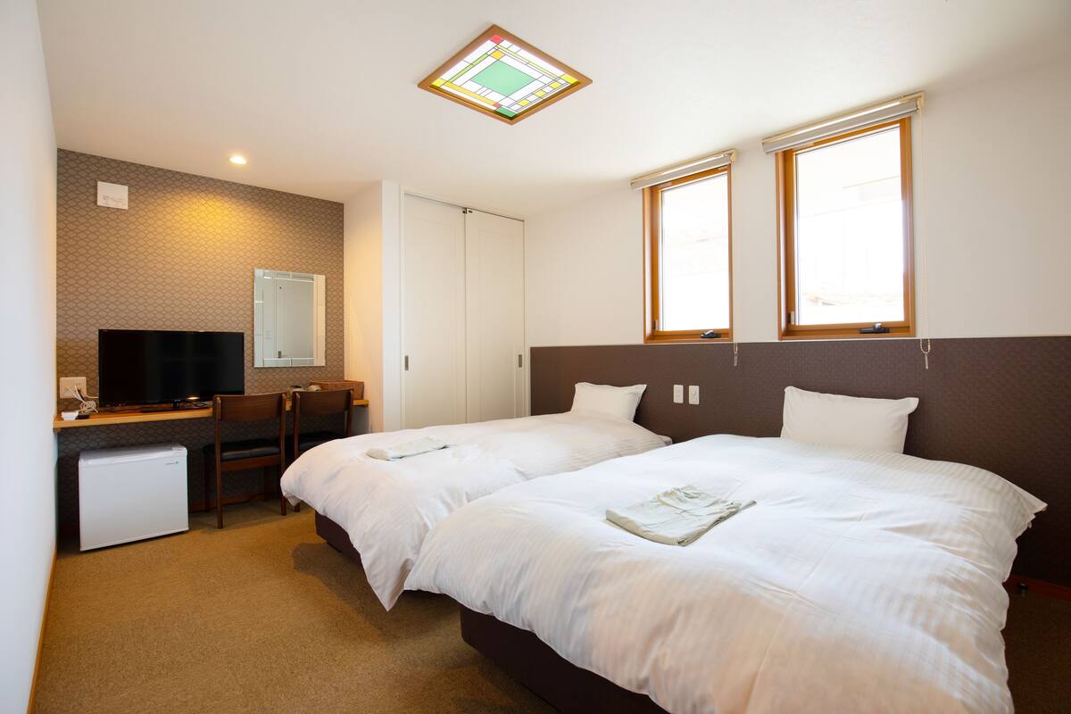 A hotel room with two beds, a desk with a computer, a TV, and a small fridge.