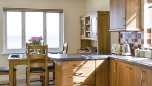 Une cuisine avec des meubles en bois, une table à manger avec des chaises, une fenêtre avec vue et un îlot de cuisine équipé d’une bouilloire.