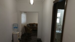 Ein schmaler Flur mit Wasserspender, einer Couch und einem durchgehenden Türrahmen sichtbaren Badezimmer.