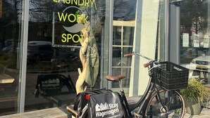 Una bicicleta estacionada frente a un edificio con un letrero que dice "Laundry Work Spot" y "Short Stay Wageningen".