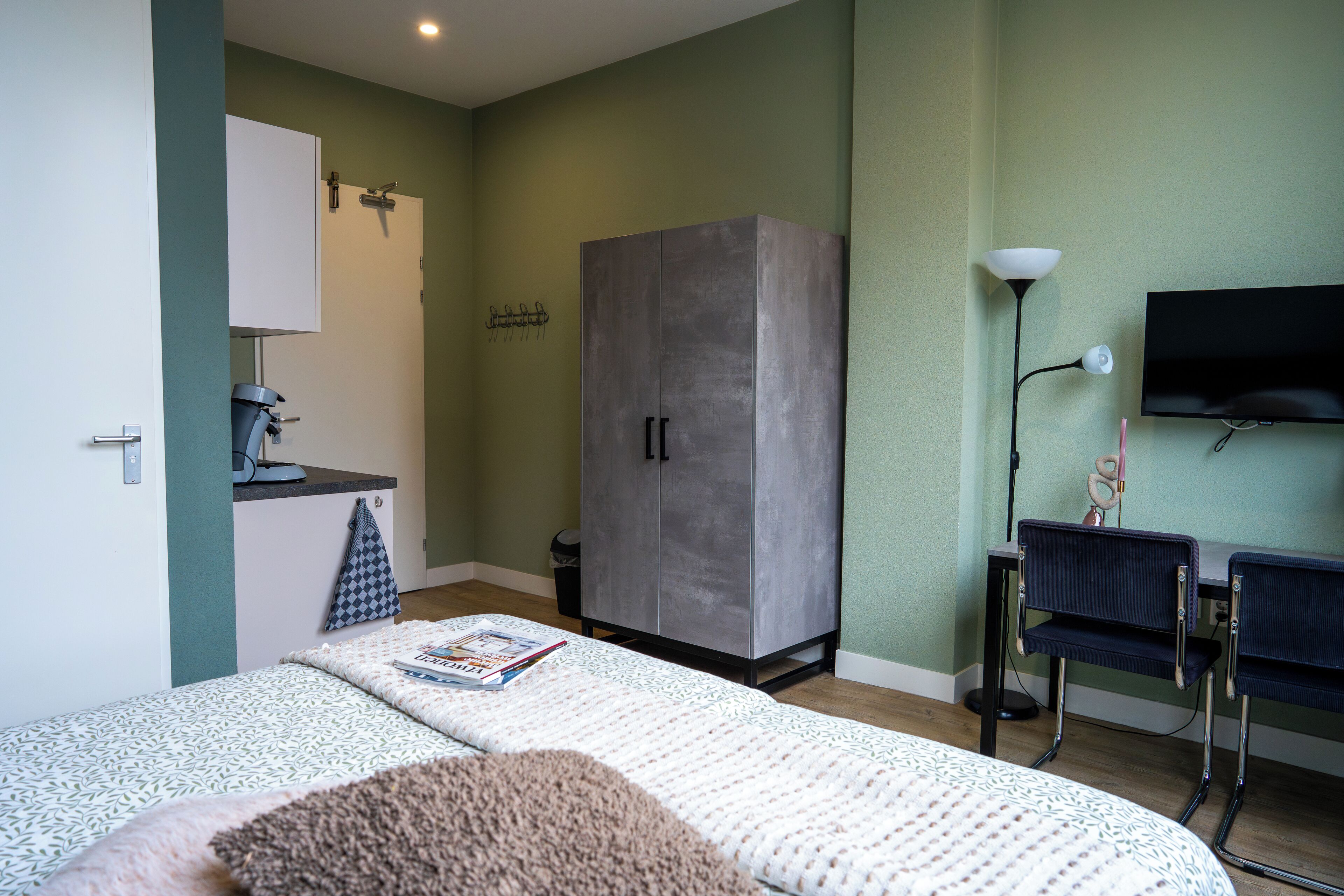 Un dormitorio con cama, armario, escritorio con silla, televisor y lámpara.