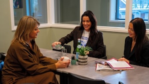 Tres personas sentadas en una mesa con una planta, un vaso y una carpeta.