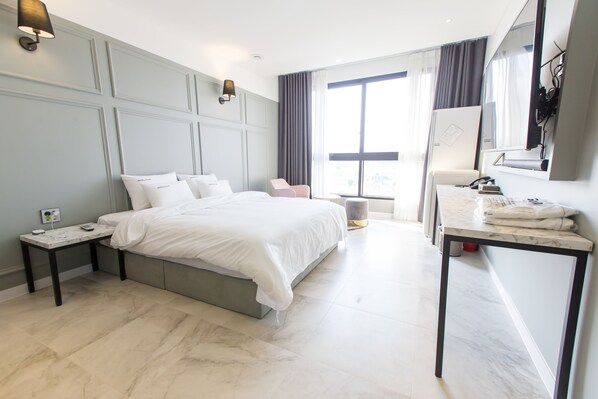 A modern hotel room with a large bed, a bedside table, a desk with a chair, and a large window with curtains. - Hotel RAUM (Suncheon)