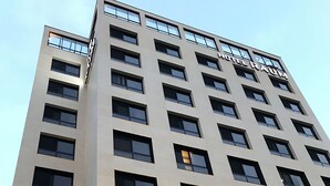A hotel building with a sign reading "HOTEL RAUM" and a ground-level establishment named "AT WOSOME PLACE". - Hotel RAUM (Suncheon)