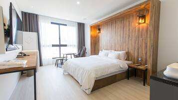 A modern hotel room with a large bed, a desk, a chair, a small table, and a wooden accent wall with a wall-mounted light.
