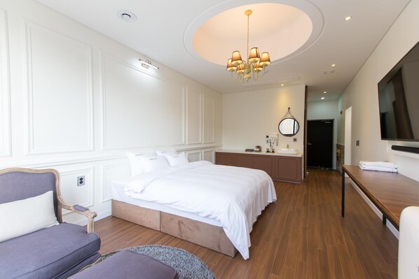 A modern hotel room with a large bed, a seating area with a sofa, a wooden table, and a TV mounted on the wall. - Hotel RAUM (Suncheon)