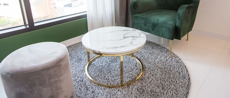Una habitación con un sillón verde, una mesa redonda de mármol y un reposapiés gris.