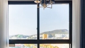 A room with a large window offering a view of a cityscape, a round table, and a chair. - Hotel RAUM (Suncheon)