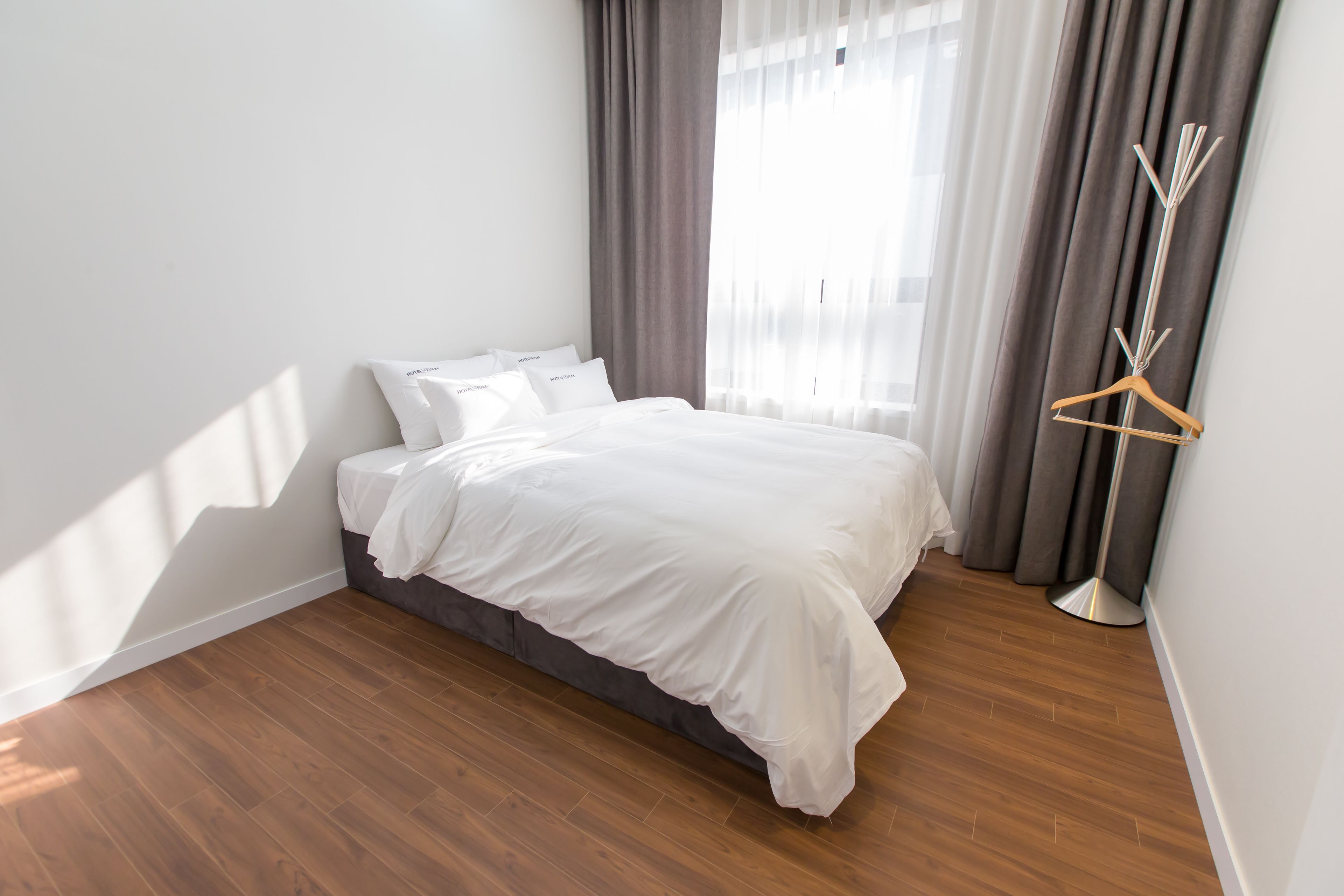 Ein ordentlich bezogenes Bett in einem Zimmer mit Holzboden, einem Nachttisch und einer Stehlampe.