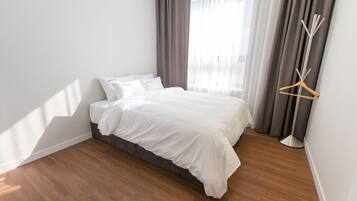 Ein ordentlich bezogenes Bett in einem Zimmer mit Holzboden, einem Nachttisch und einer Stehlampe.