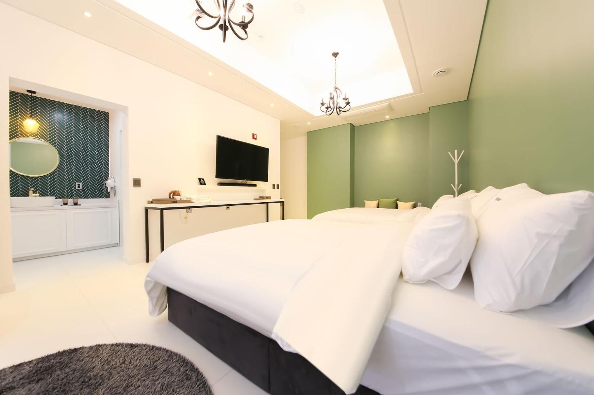 A modern bedroom with a bed, a TV, a desk, and a bathroom.