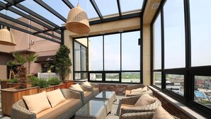 A rooftop terrace with wicker furniture, large windows, and a view of the cityscape. - Hotel RAUM (Suncheon)