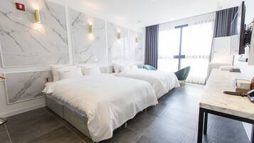 Ett hotellrum med två sängar, väggpaneler i marmor, ett stort fönster med gardiner och ett skrivbord med en spegel.