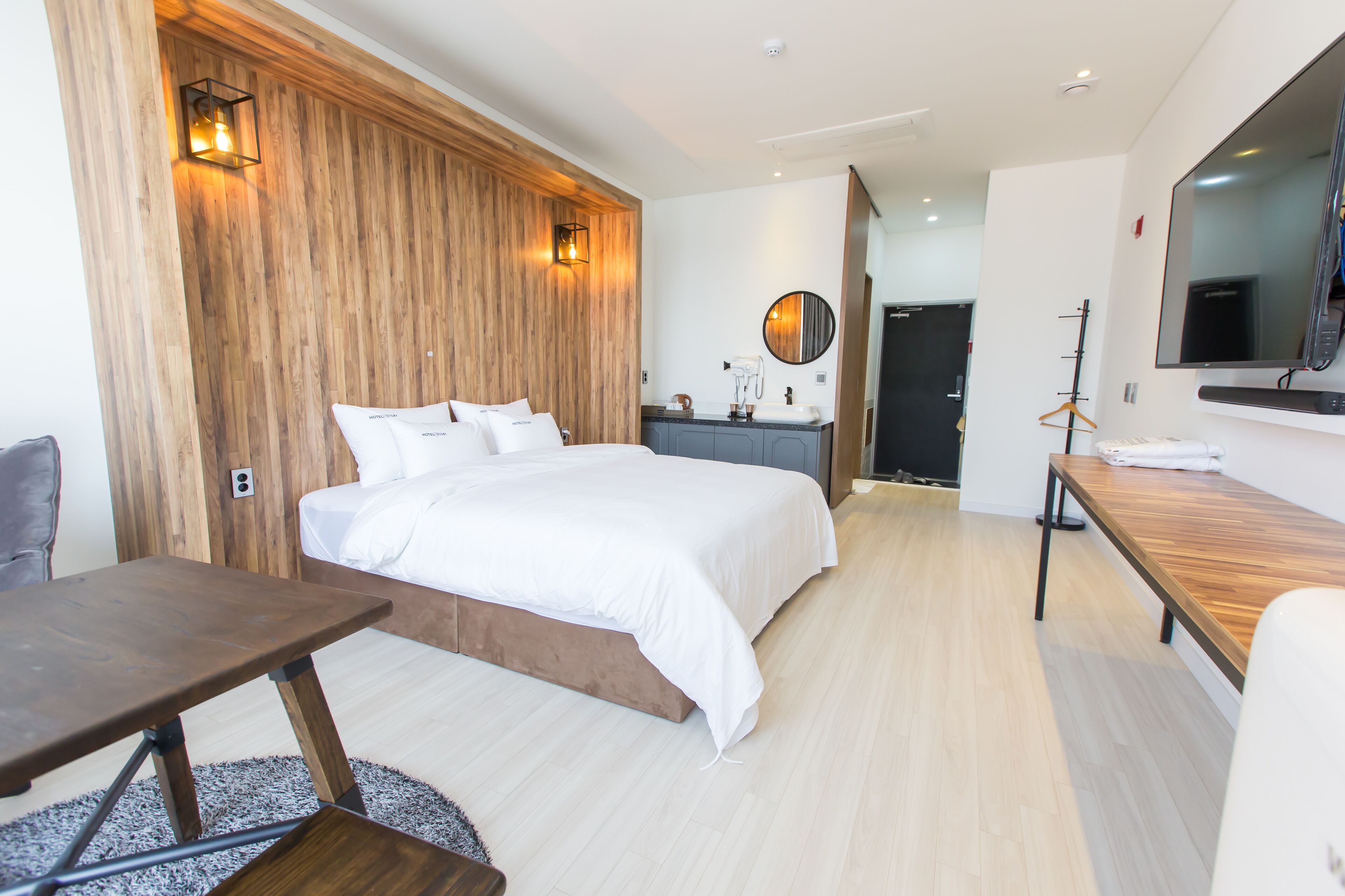A modern hotel room with a wooden accent wall, a large bed, a desk, and a mirror.