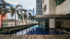 A modern hotel with a rooftop pool, palm trees, and a view of a tall building. - OYO Home 580 Luxury 2 Bedroom Taragon Puteri (Kuala Lumpur)