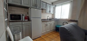 A kitchen with white cabinets, a microwave, a refrigerator, a sink, and a window with curtains.