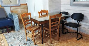 A dining area with a glass-top table, wooden chairs, a black chair, and a patterned rug.
