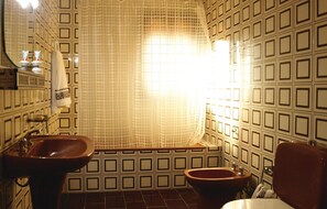 Ein Badezimmer mit gefliesten Wänden, einer Badewanne, zwei Waschbecken und einer Toilette.