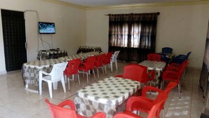 Une salle de conférence équipée de plusieurs tables et chaises, d’un téléviseur fixé au mur et d’une fenêtre avec des rideaux.