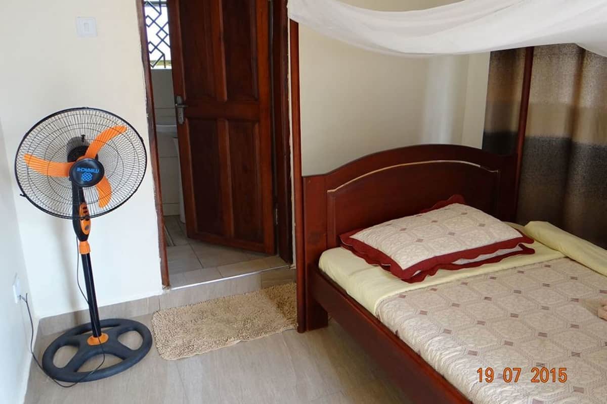 Ein Schlafzimmer mit einem hölzernen Bett, einem Standventilator und einem weißen Baldachin.