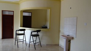 Une pièce avec un comptoir incurvé, deux tabourets de bar, un évier et une porte.