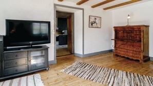 A living room with a flat-screen TV on a cabinet, a wooden cabinet, a rug, and a painting on the wall.